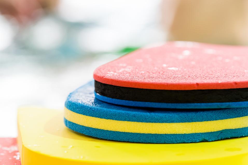 Bunte Schwimmbretter in verschiedenen Farben übereinander gestapelt, mit Wassertropfen auf der Oberfläche.